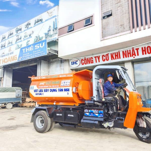 Xe ô tô trộn bê tông nhựa nóng màu cam trước cửa công ty cơ khí Nhật Hoàng, phương tiện xây dựng chuyên nghiệp, vận hành dễ dàng, cung cấp vật liệu xây dựng chất lượng cao tại Nam Định.